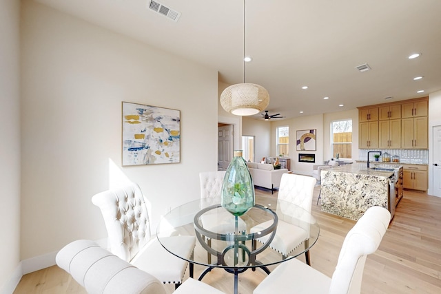 dining room with a glass covered fireplace, visible vents, light wood finished floors, and recessed lighting