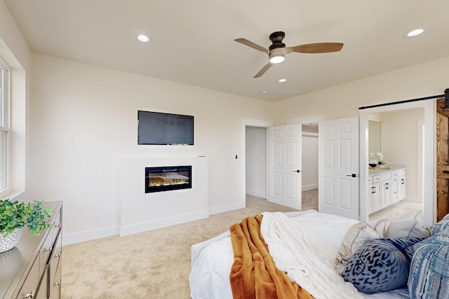 bedroom featuring a barn door, recessed lighting, light carpet, baseboards, and a glass covered fireplace