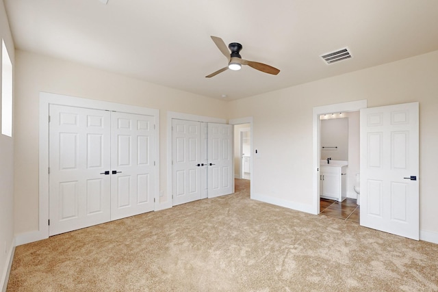 unfurnished bedroom featuring ensuite bathroom, carpet floors, visible vents, baseboards, and two closets