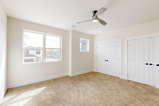 unfurnished bedroom featuring two closets, baseboards, light colored carpet, and visible vents