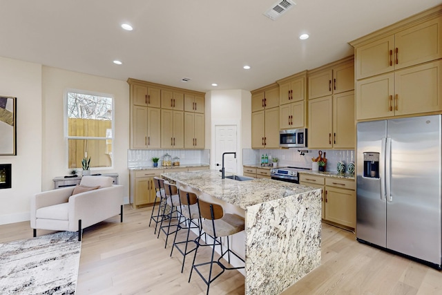 kitchen with a sink, light wood finished floors, light stone countertops, appliances with stainless steel finishes, and visible vents