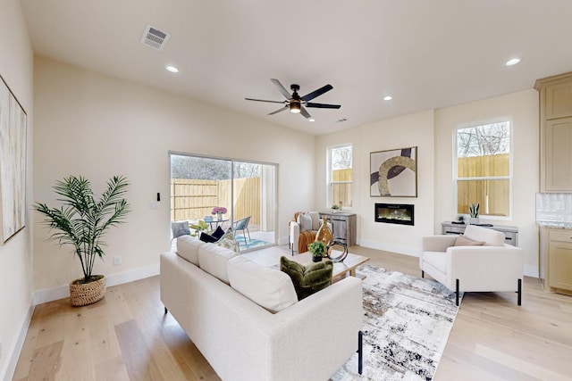 living area featuring recessed lighting, visible vents, a glass covered fireplace, light wood-type flooring, and baseboards