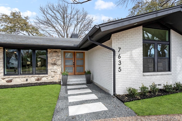 view of exterior entry with french doors, brick siding, a yard, a chimney, and stone siding