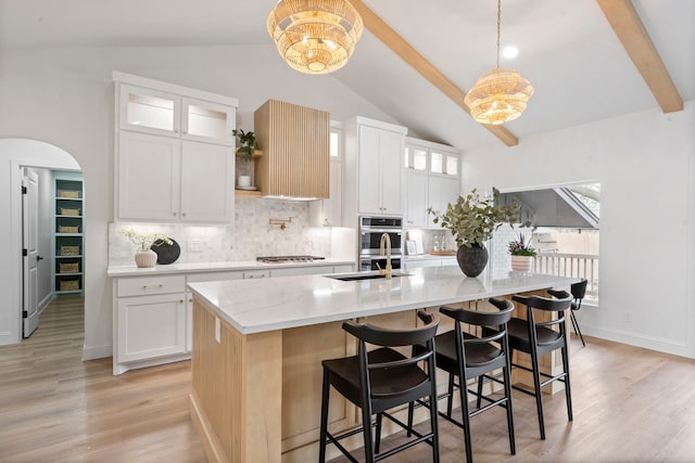 kitchen featuring light wood-style floors, arched walkways, vaulted ceiling with beams, and a sink