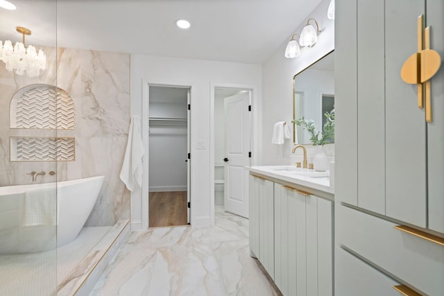 bathroom with marble finish floor, a walk in closet, vanity, a freestanding tub, and a notable chandelier