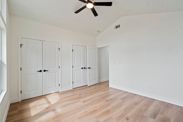 unfurnished bedroom featuring two closets, lofted ceiling, visible vents, light wood-style floors, and baseboards