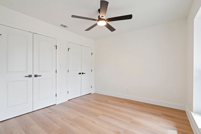 unfurnished bedroom featuring baseboards, light wood-style floors, visible vents, and multiple closets