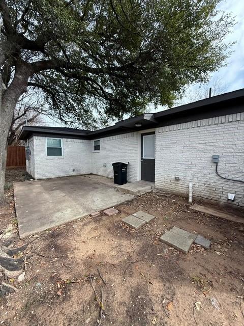 rear view of property with crawl space, brick siding, fence, and a patio