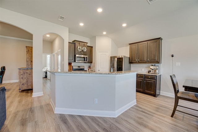 kitchen with light wood finished floors, visible vents, arched walkways, light stone countertops, and stainless steel appliances