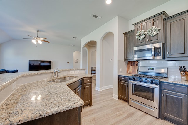 kitchen with appliances with stainless steel finishes, backsplash, light wood-type flooring, and a sink