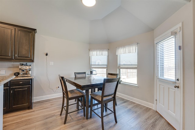 dining room featuring lofted ceiling, light wood finished floors, and baseboards