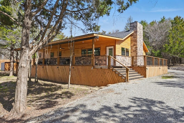 exterior space with stairway, a chimney, stone siding, a wooden deck, and ceiling fan