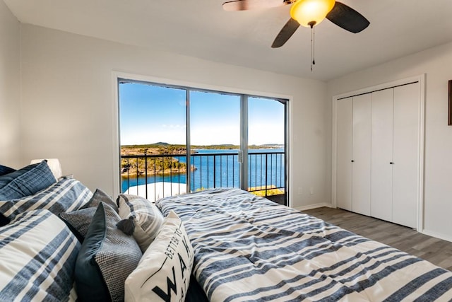 bedroom with baseboards, ceiling fan, wood finished floors, a water view, and access to outside