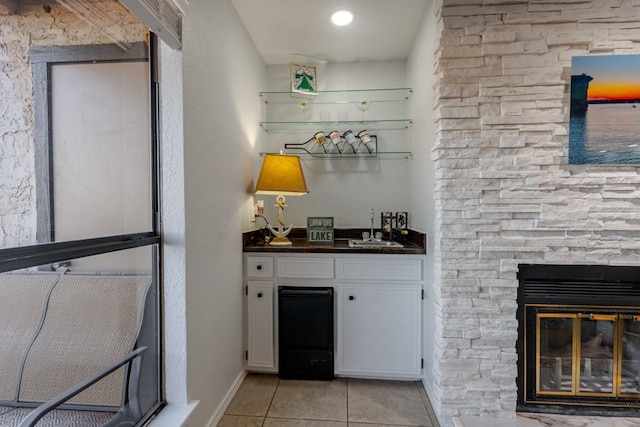 bar featuring light tile patterned floors, baseboards, a sink, a fireplace, and indoor wet bar