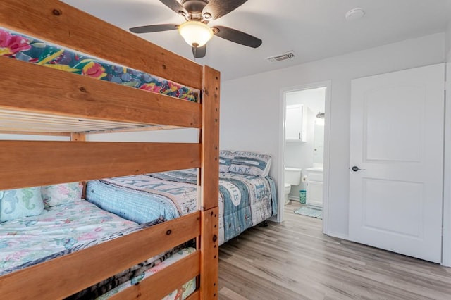 bedroom with baseboards, visible vents, ensuite bath, ceiling fan, and wood finished floors