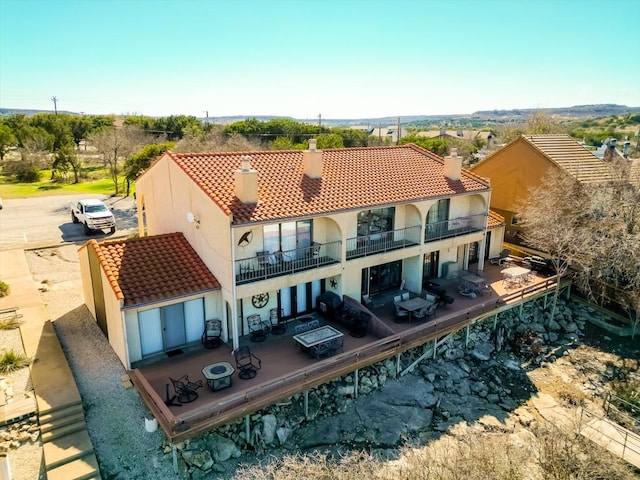 back of property with a chimney, a tiled roof, a balcony, and stucco siding