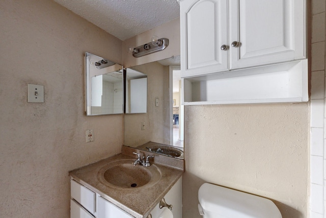 bathroom with a textured wall, a textured ceiling, vanity, and toilet