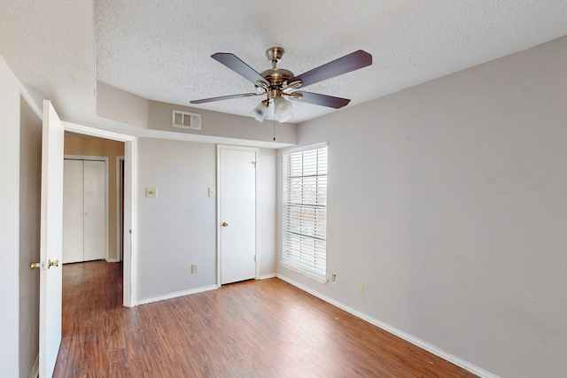 unfurnished bedroom featuring visible vents, baseboards, a textured ceiling, and wood finished floors