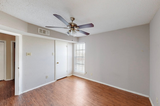 unfurnished bedroom with visible vents, a textured ceiling, baseboards, and wood finished floors