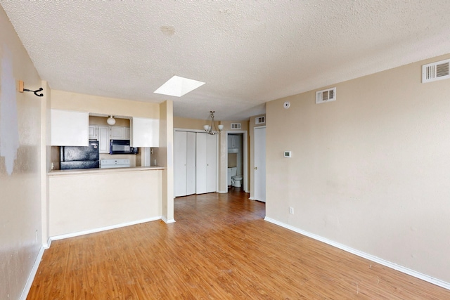 unfurnished living room featuring a skylight, baseboards, visible vents, and light wood-type flooring