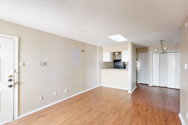 unfurnished living room featuring light wood-type flooring, baseboards, and a textured ceiling