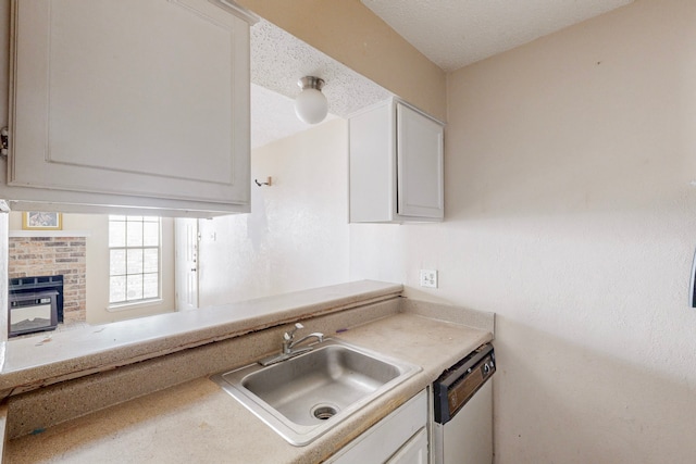 kitchen with white dishwasher, a sink, light countertops, white cabinets, and a textured ceiling