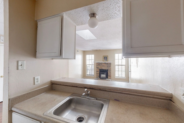 kitchen with a skylight, a sink, a textured ceiling, a brick fireplace, and a textured wall