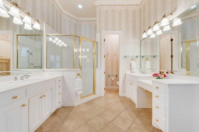 full bathroom with wallpapered walls, a stall shower, toilet, a sink, and two vanities