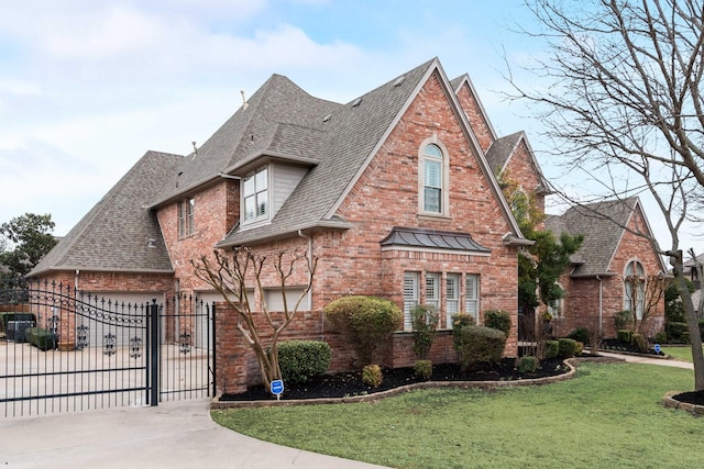 tudor house featuring brick siding, concrete driveway, a gate, fence, and a front yard