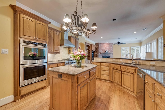 kitchen featuring wall chimney range hood, crown molding, appliances with stainless steel finishes, and a sink