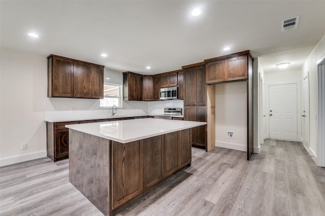 kitchen featuring visible vents, light wood-style flooring, a center island, stainless steel appliances, and a sink