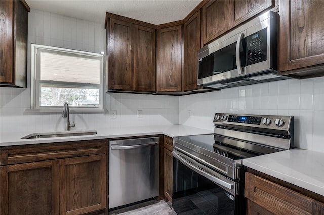 kitchen with dark brown cabinets, appliances with stainless steel finishes, a sink, and tasteful backsplash