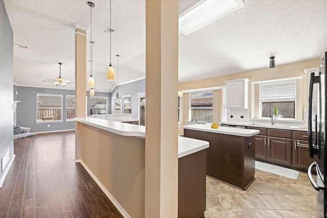 kitchen featuring dark brown cabinetry, a sink, a kitchen island, open floor plan, and light countertops