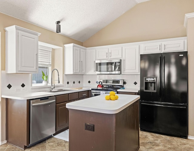 kitchen featuring stainless steel appliances, light countertops, white cabinets, vaulted ceiling, and a sink