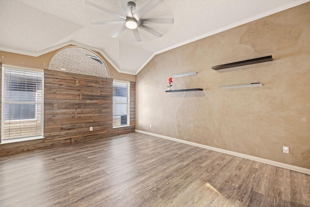 empty room with a ceiling fan, ornamental molding, wood finished floors, vaulted ceiling, and a textured ceiling