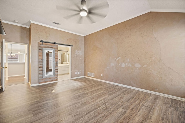 empty room with wood finished floors, visible vents, crown molding, and a barn door