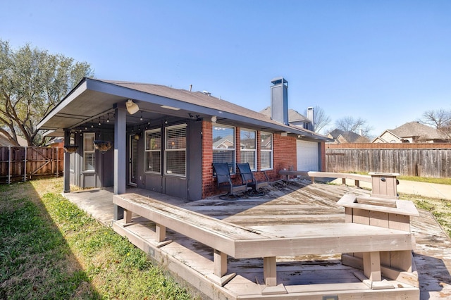 back of property featuring brick siding, a chimney, a garage, a fenced backyard, and a wooden deck