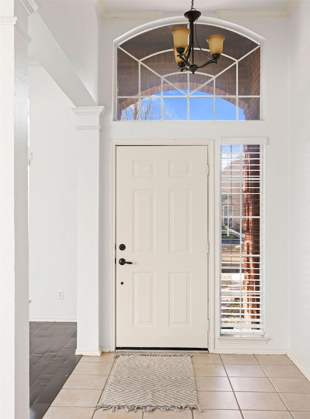 tiled entrance foyer featuring ornamental molding, a notable chandelier, and baseboards