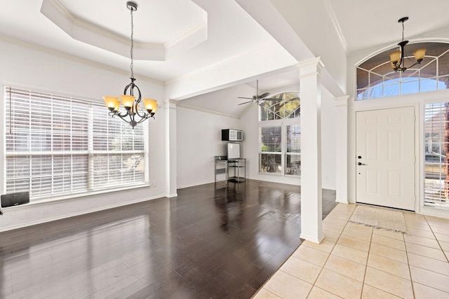 foyer entrance with ceiling fan with notable chandelier, a tray ceiling, a healthy amount of sunlight, and ornate columns