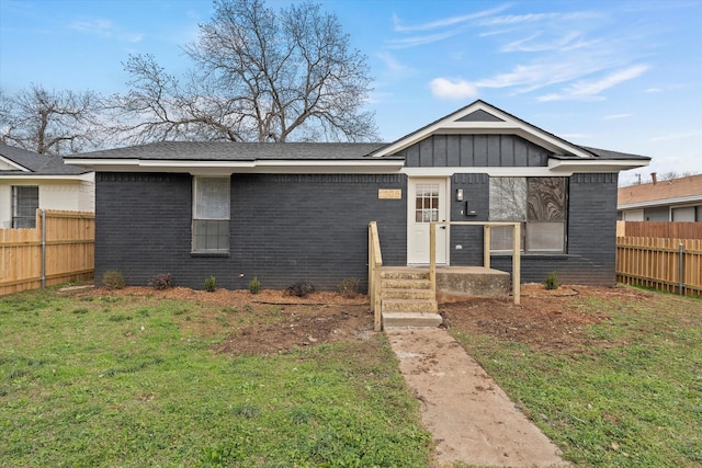 view of front of house featuring fence, a front lawn, board and batten siding, and brick siding