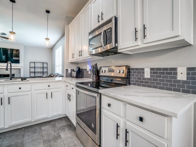 kitchen with light stone counters, stainless steel appliances, a sink, white cabinetry, and pendant lighting