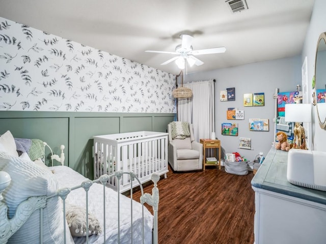 bedroom with wallpapered walls, visible vents, dark wood finished floors, a wainscoted wall, and ceiling fan