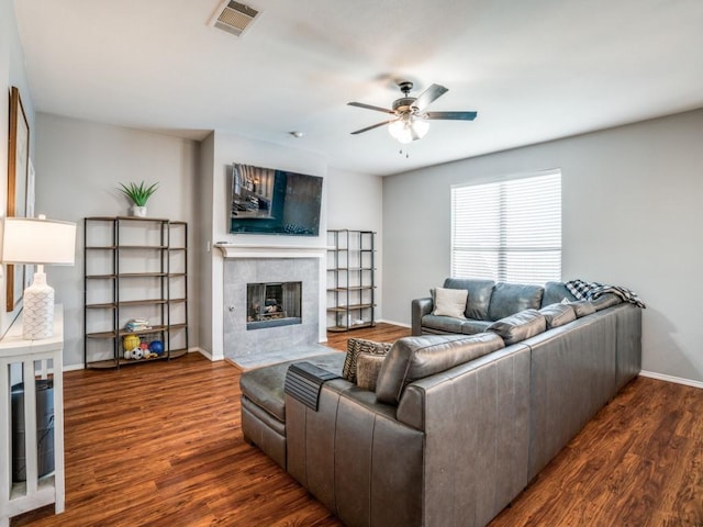 living area with visible vents, ceiling fan, a tiled fireplace, and wood finished floors