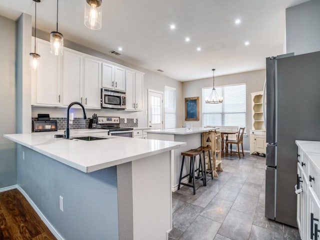 kitchen featuring a breakfast bar area, stainless steel appliances, visible vents, white cabinetry, and a peninsula