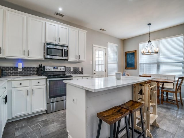 kitchen with tasteful backsplash, white cabinets, appliances with stainless steel finishes, a breakfast bar area, and a center island