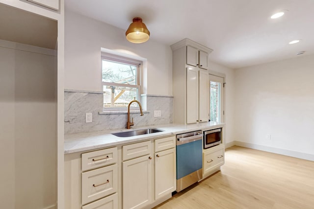 kitchen with light wood-type flooring, appliances with stainless steel finishes, backsplash, and a sink