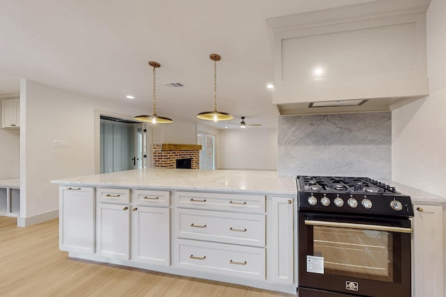 kitchen featuring a fireplace, light stone countertops, gas range, and white cabinets