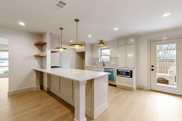 kitchen with a peninsula, visible vents, appliances with stainless steel finishes, light wood-type flooring, and decorative backsplash