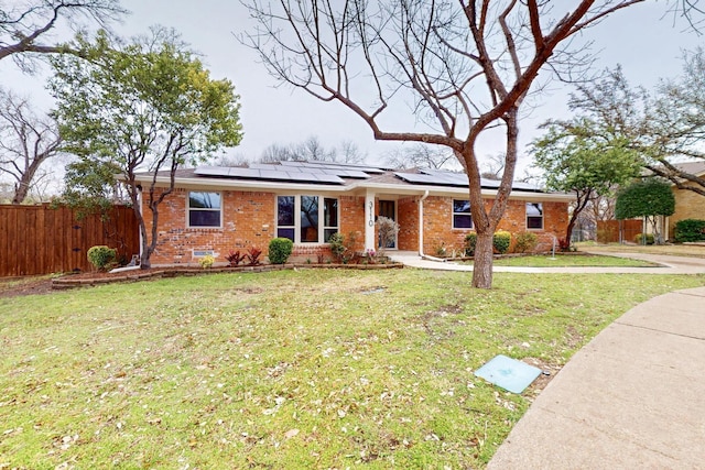 ranch-style house featuring a front yard, fence, solar panels, and brick siding