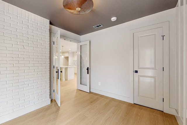 unfurnished bedroom with baseboards, visible vents, light wood-style flooring, and brick wall